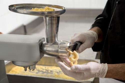 A chef in a professional kitchen prepares fresh pasta using a pasta extruder, showcasing culinary craftsmanship ideal for food enthusiasts exploring authentic cooking techniques.
