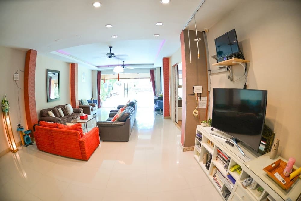 A spacious, modern living room with glossy white floors, vibrant orange and gray sofas, a mounted TV, and a view of the outdoors through large glass doors, ideal for travelers seeking a cozy yet stylish accommodation.