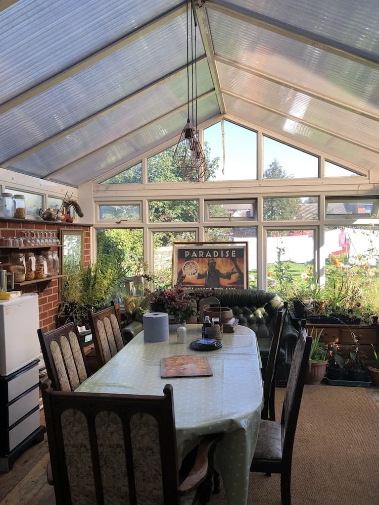 A cozy conservatory filled with natural light, lush greenery, and a dining setup creates an inviting atmosphere perfect for relaxing meals or family gatherings.