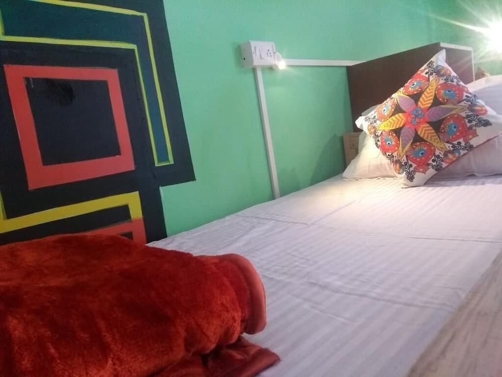 A cozy bedroom with vibrant green walls, colorful geometric art, and a neatly made bed adorned with patterned pillows invites travelers seeking a comfortable and artistic retreat.