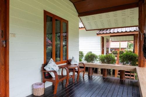 A cozy wooden porch with comfortable seating and lush greenery exudes a tranquil atmosphere, perfect for a relaxing getaway at a rustic retreat.