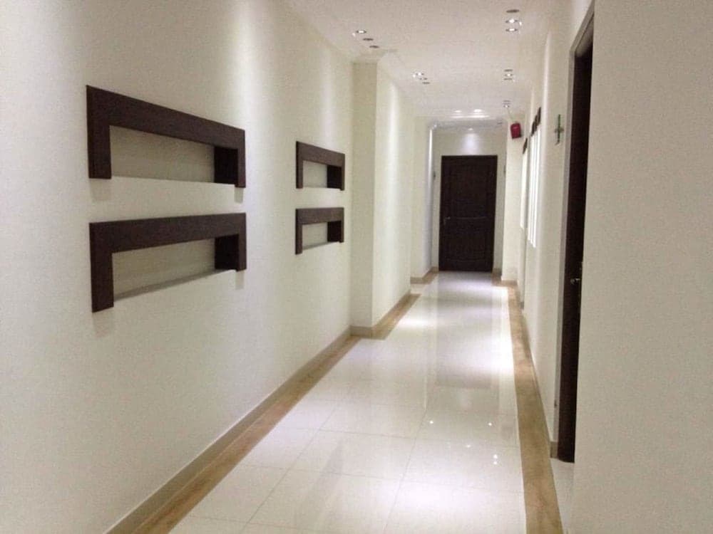 A serene hotel corridor features minimalist decor with dark wooden shelves against white walls, polished tiles, and soft lighting, ideal for travelers seeking a calm and modern accommodation experience.