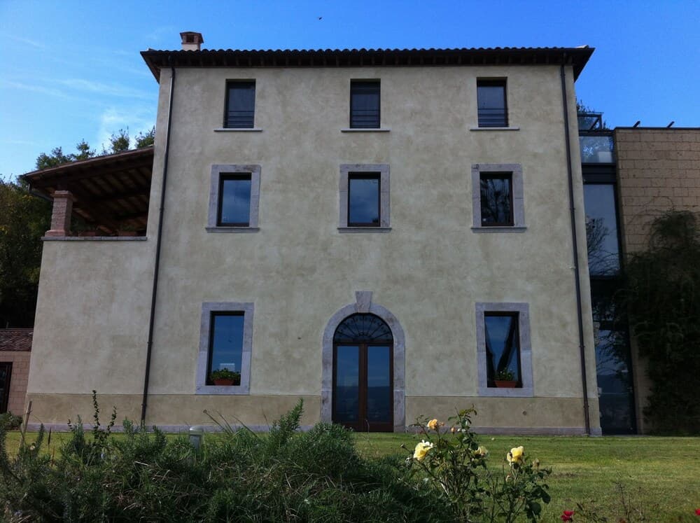 A serene countryside villa with a rustic facade, arched doorway, and lush greenery offers an idyllic retreat for travelers seeking relaxation and natural beauty.