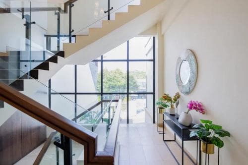 A modern, airy interior hallway featuring a sleek staircase, large windows overlooking greenery, vibrant floral arrangements, and a stylish console table, ideal for showcasing contemporary home design in real estate listings.