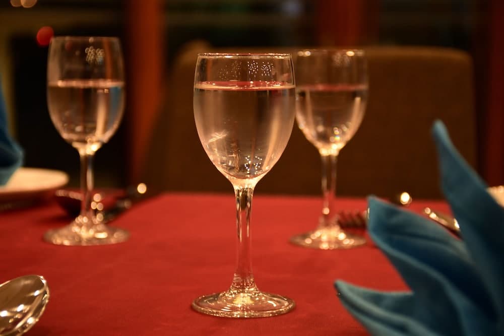 A warmly lit dining table set with elegant wine glasses, blue napkins, and a red tablecloth creates an inviting atmosphere perfect for a romantic dinner or special occasion.