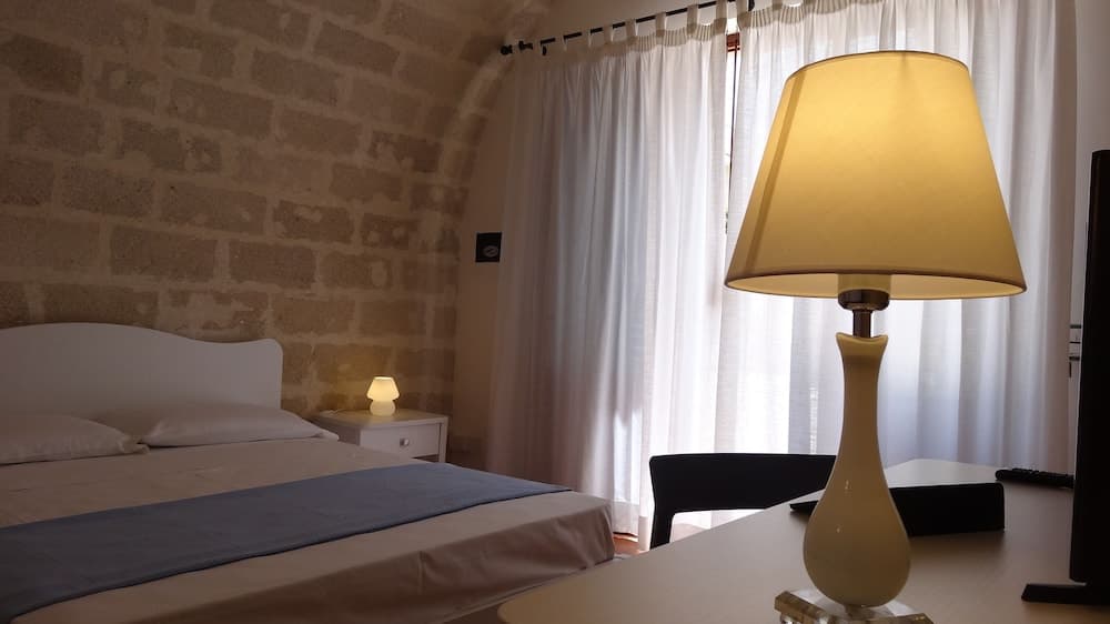 A cozy hotel room with a rustic stone wall, soft lighting from table lamps, white curtains diffusing natural light, and neatly arranged furniture creates a serene atmosphere ideal for relaxation and leisure travel.