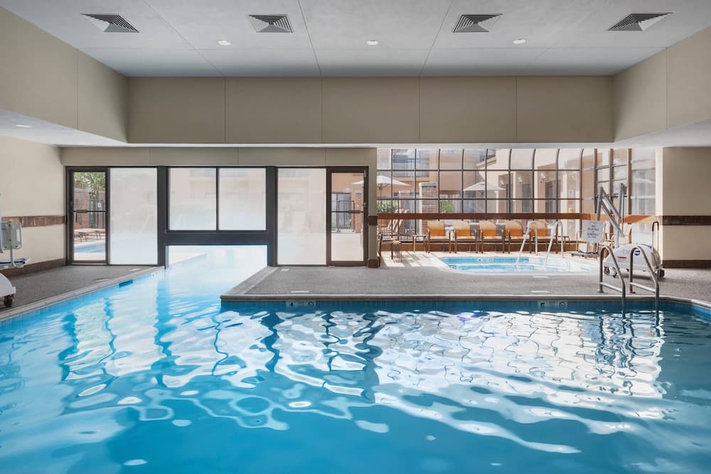 A serene indoor swimming pool area with clear blue water, modern design, large windows, lounge chairs, and umbrellas offers a relaxing retreat for travelers seeking leisure and comfort.