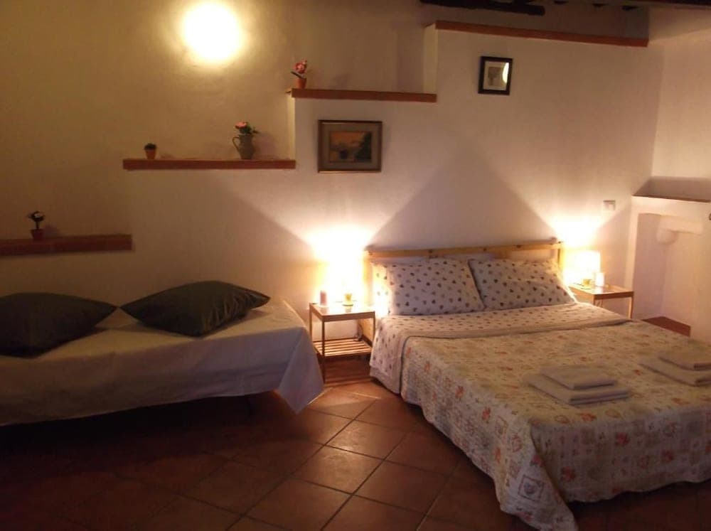 A cozy bedroom with warm lighting, tiled floors, two inviting beds adorned with patterned linens, and rustic shelves displaying small decorative items creates an intimate atmosphere ideal for travelers seeking a comfortable and charming accommodation.