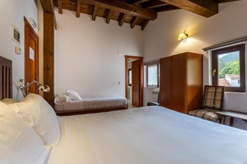 A cozy rustic bedroom with wooden beams, a scenic view through the window, and simple furnishings offers a serene retreat for travelers seeking relaxation in a countryside setting.