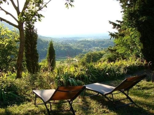 A serene garden retreat features two lounge chairs overlooking lush greenery and distant hills, ideal for relaxation and nature-inspired travel experiences.