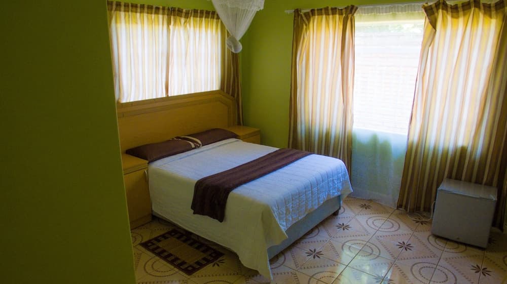 A cozy hotel room with vibrant green walls, patterned curtains, and tiled floors offers a serene retreat for travelers seeking comfort and simplicity.