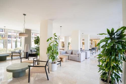 A bright, modern hotel lobby features sleek furniture, lush green plants, and large windows, creating an inviting atmosphere ideal for travelers seeking comfort and style.