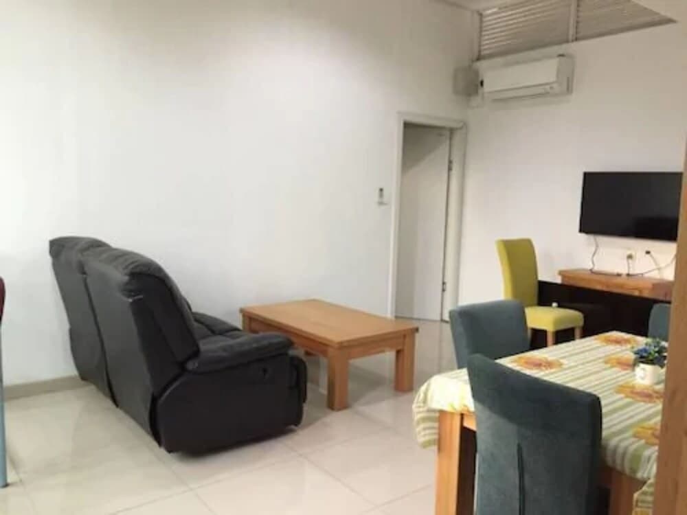 A cozy apartment living room features a black recliner, wooden coffee table, colorful chairs, and a flat-screen TV, creating a welcoming atmosphere ideal for travelers seeking comfort and convenience.