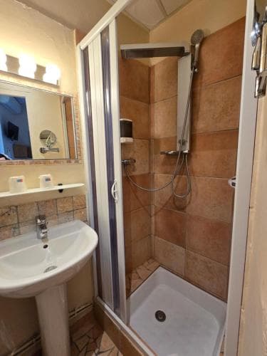 A cozy hotel bathroom features a tiled shower enclosure, a white pedestal sink, and a mirror-lit vanity, creating a warm and inviting atmosphere ideal for travelers seeking comfort and cleanliness.