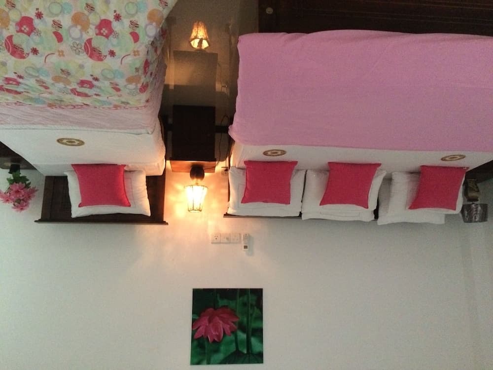 A cozy hotel room features two neatly arranged beds with pink and floral bedding, warm wall-mounted lamps, and a serene lotus painting, ideal for travelers seeking comfort and tranquility.