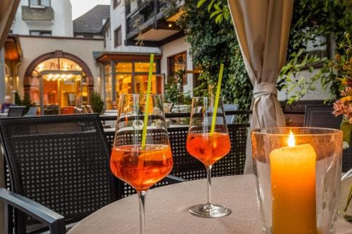 A cozy outdoor café scene features two glasses of Aperol Spritz on a table with a lit candle, set against the backdrop of warmly lit buildings, ideal for a romantic evening or a relaxing getaway.