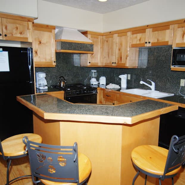 A cozy kitchen with wooden cabinets, granite countertops, and bar stools offers a warm and inviting atmosphere ideal for family gatherings or vacation rentals.