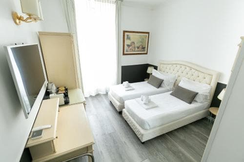 A cozy hotel room features two neatly made beds, a vanity with a mirror, soft lighting, and a framed artwork, creating a welcoming atmosphere ideal for travelers seeking comfort and relaxation.