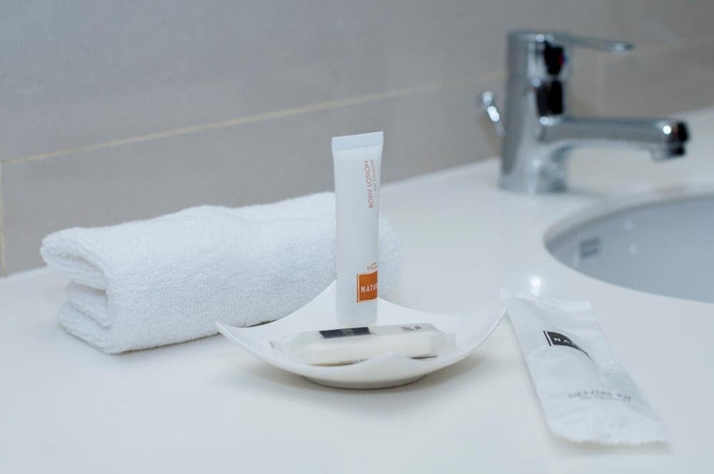 A serene hotel bathroom scene features a neatly folded white towel, a tube of body lotion, and toiletries on a pristine countertop, ideal for travelers seeking comfort and cleanliness.