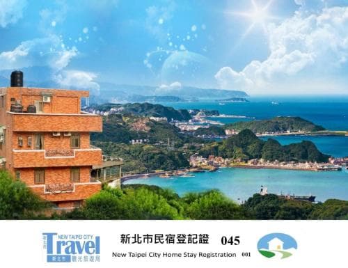 A serene coastal view featuring a brick building overlooking lush greenery and the ocean under a bright blue sky, ideal for travelers seeking a tranquil New Taipei City home stay experience.