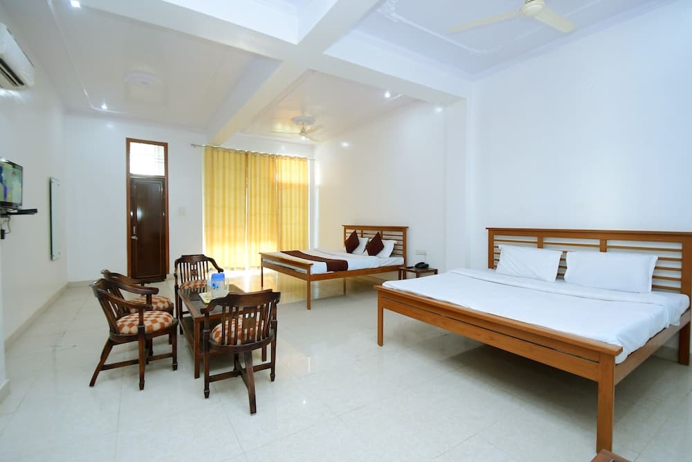 A cozy hotel room features two wooden beds, a dining table with chairs, yellow curtains, and a mounted TV, ideal for travelers seeking comfort and functionality.