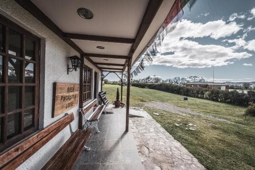 A cozy porch with wooden accents and stone flooring overlooks a serene grassy landscape under a partly cloudy sky, ideal for travelers seeking a peaceful rural retreat.
