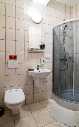 A clean, functional hotel bathroom features tiled walls, a modern shower enclosure, a sink with toiletries, and a toilet, ideal for travelers seeking basic amenities in a compact space.