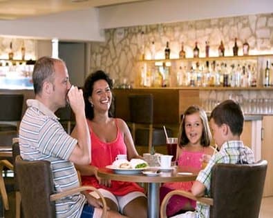 A cheerful family enjoys a meal together at a cozy restaurant bar area, surrounded by warm lighting and stocked shelves, ideal for capturing the essence of family-friendly dining experiences.
