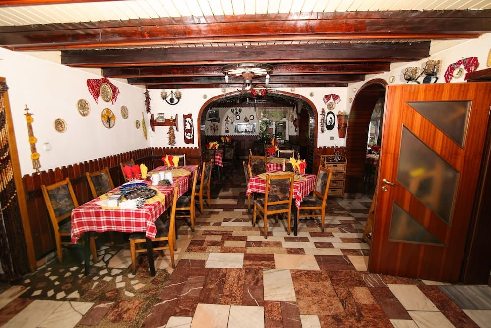 A cozy restaurant interior with rustic wooden beams, checkered tablecloths, decorative plates on the walls, and warm lighting creates an inviting atmosphere perfect for travelers seeking traditional dining experiences.