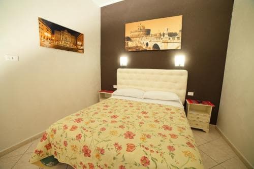 A cozy hotel room features a floral-patterned bedspread, framed cityscape artwork, and warm lighting, creating an inviting atmosphere ideal for travelers seeking comfort in urban accommodations.