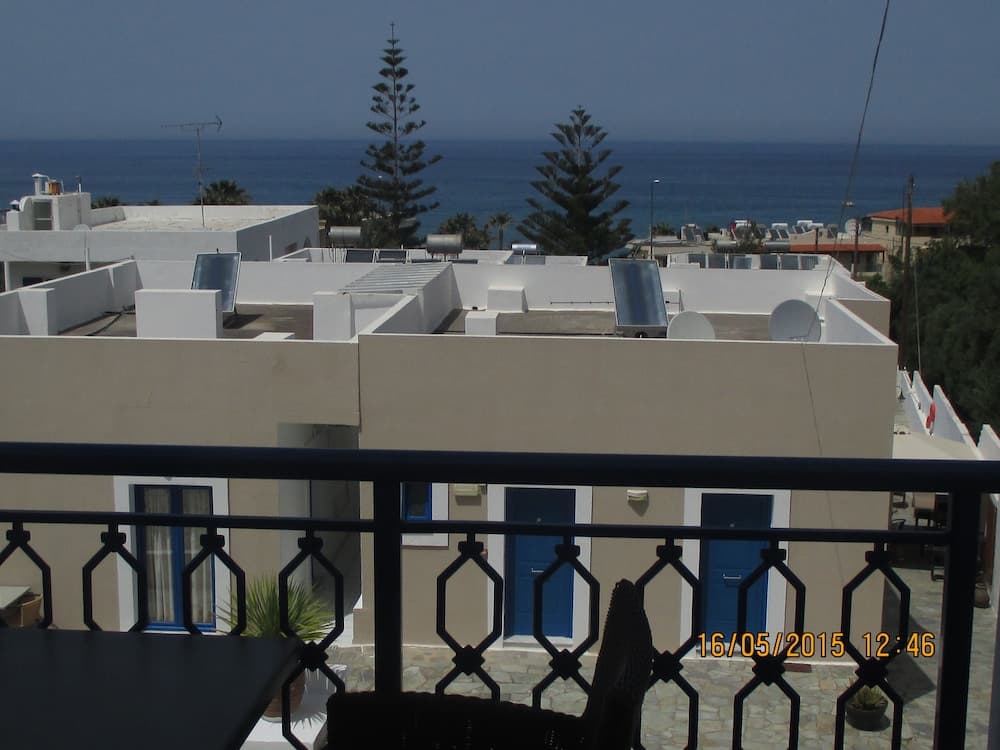 A serene coastal balcony view showcases white buildings with blue doors, solar panels, and lush greenery against the backdrop of a calm sea, ideal for travelers seeking a tranquil seaside retreat.