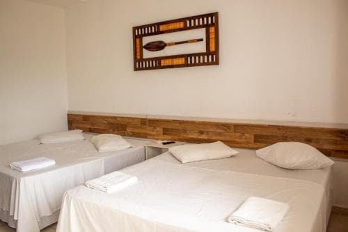 A cozy hotel room features two neatly made beds with white linens, a wooden headboard, and a decorative wall art piece, ideal for travelers seeking comfort and simplicity.