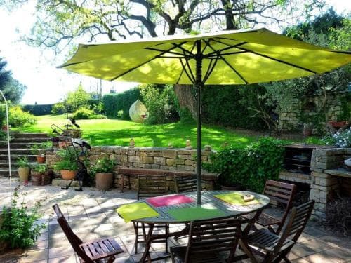 A serene outdoor patio features a vibrant lime green umbrella shading a colorful table set amidst lush greenery, ideal for relaxing garden getaways.