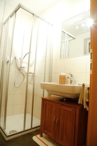 A cozy hotel bathroom features a glass-enclosed shower, wooden vanity cabinet, and tiled walls, creating a clean and inviting atmosphere ideal for travelers seeking comfort and functionality.