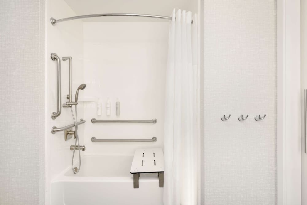 A clean, accessible bathroom features a white bathtub equipped with safety bars, a shower seat, and toiletries, ideal for travelers seeking comfort and convenience in accommodations.
