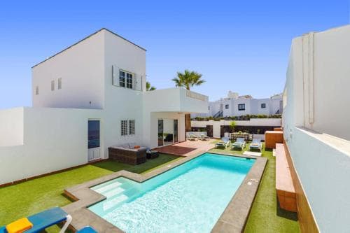 A serene Mediterranean-style villa features a vibrant blue pool surrounded by lush greenery and lounge chairs, ideal for a relaxing vacation getaway.