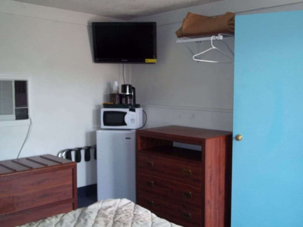 A cozy motel room features a neatly made bed, wooden furniture, a mounted TV, and a small kitchenette with a microwave and coffee maker, ideal for budget travelers seeking comfort and convenience.