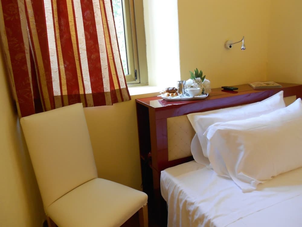 A cozy hotel room features a neatly made bed beside a wooden desk adorned with fresh flowers and breakfast items, set against warm yellow walls and patterned curtains, ideal for travelers seeking comfort and convenience.
