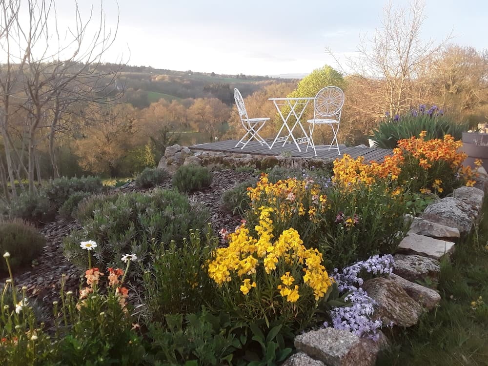 A serene garden terrace with vibrant yellow flowers, white chairs, and a scenic view of rolling hills offers a tranquil retreat for nature lovers seeking peaceful relaxation.