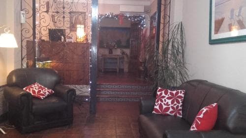 A cozy living room with leather sofas adorned with red-patterned cushions, festive string lights, and ornate ironwork creates a warm, inviting atmosphere ideal for travelers seeking a comfortable stay in a charming, homey setting.