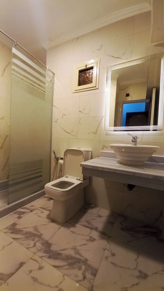 A luxurious bathroom with marble walls and flooring features a modern sink, toilet, and glass-enclosed shower, ideal for travelers seeking upscale accommodations.