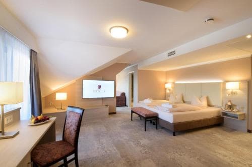 A cozy hotel room with a king-sized bed, modern furnishings, and a mounted TV creates a serene atmosphere ideal for travelers seeking relaxation and comfort during their stay.