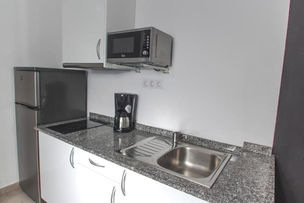 A modern, compact kitchenette featuring white cabinets, a granite countertop, stainless steel sink, microwave, coffee maker, and refrigerator, ideal for travelers seeking self-catering accommodations.