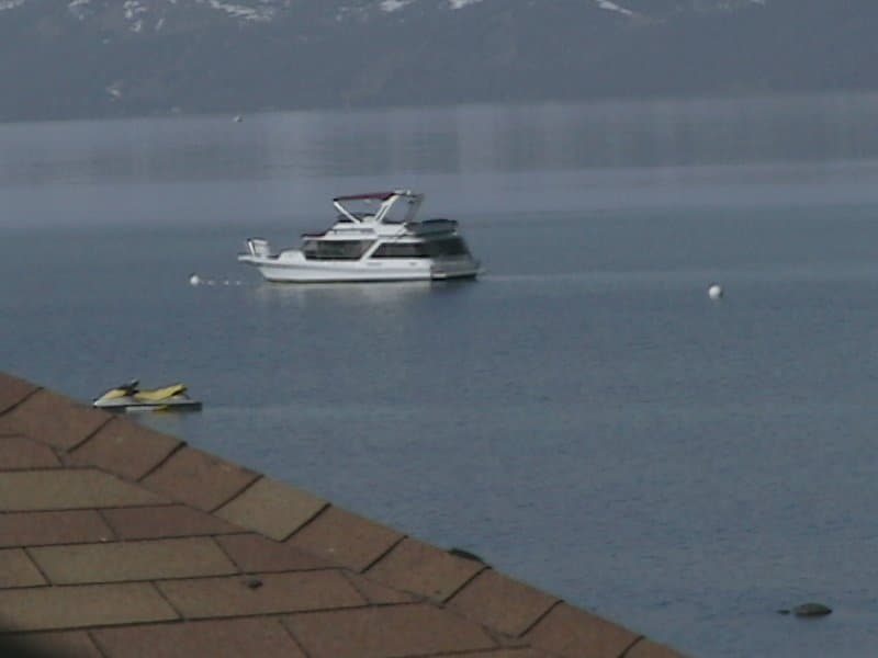 A serene lakeside scene features a motorboat anchored on calm waters near a tiled-roof shoreline, ideal for tranquil boating getaways amidst misty mountain views.