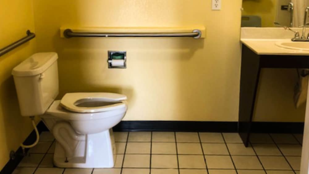 A clean, accessible bathroom with yellow walls, grab bars, tiled flooring, and a sink offers a functional space ideal for travelers needing mobility assistance.