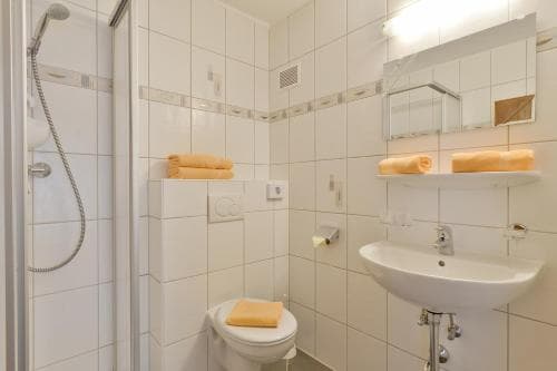 A clean, compact bathroom with white tiled walls, a shower, sink, toilet, and neatly folded orange towels creates a functional and inviting space ideal for travelers seeking comfort in accommodations.