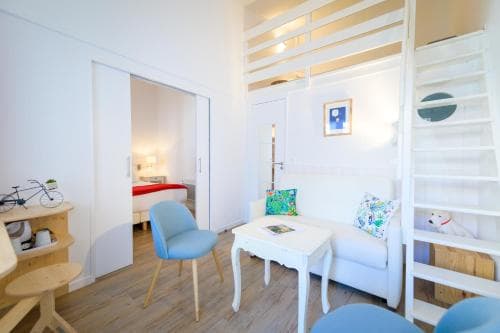 A cozy, modern studio apartment features a bright white interior with wooden accents, a comfortable seating area, and a loft bed, ideal for travelers seeking a stylish and compact urban retreat.