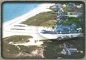 An aerial view captures a serene coastal village with charming houses nestled among lush greenery beside a pristine sandy beach, ideal for travelers seeking a tranquil seaside retreat.