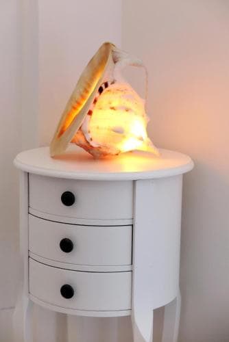 A cozy corner features a glowing seashell lamp atop a white side table, creating a serene and inviting atmosphere ideal for relaxation or home decor inspiration.