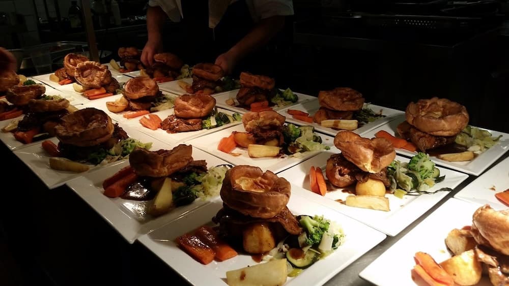 A bustling restaurant kitchen showcases an array of beautifully plated roast dinners with Yorkshire puddings, vegetables, and gravy, creating a warm and inviting atmosphere perfect for culinary enthusiasts seeking a gourmet dining experience.